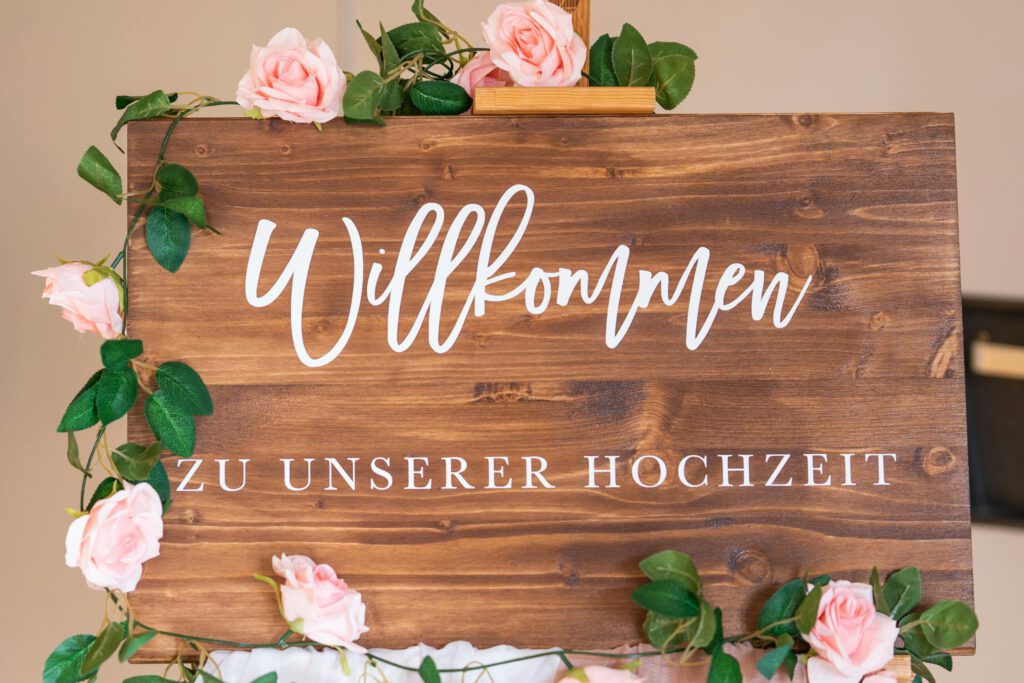 Wooden welcome sign adorned with pink roses for a wedding celebration.